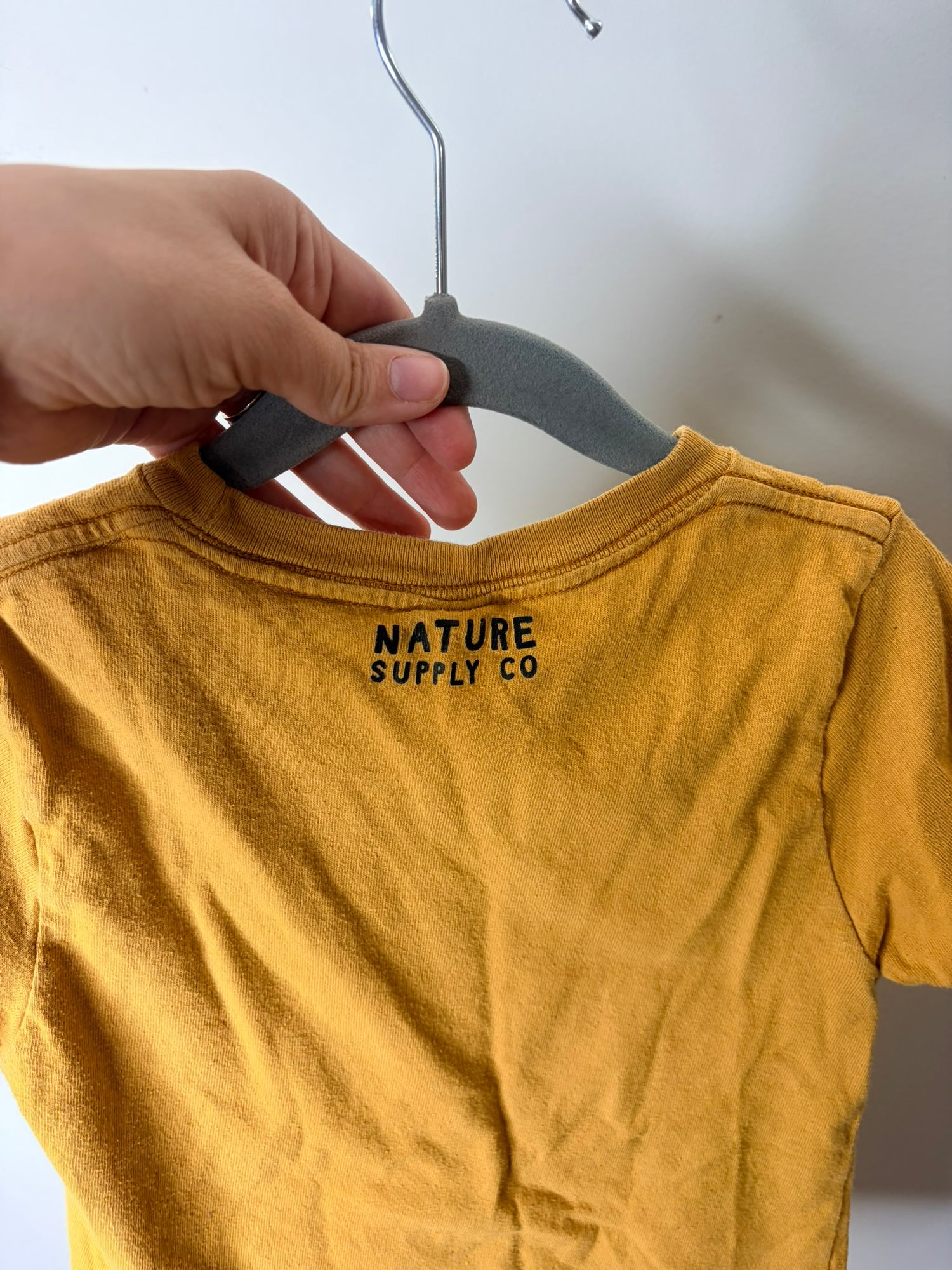 Mustard yellow T-shirt with 'Save The Bees' text and bee graphic, hanging on a hanger.