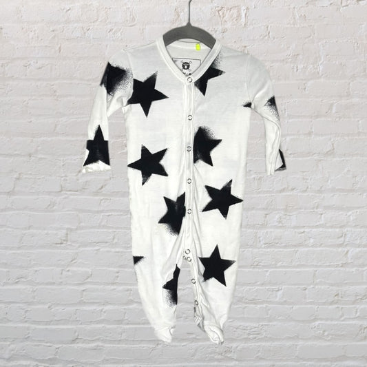 White baby onesie with black star print, featuring snap buttons down the front, hanging on a hanger against a brick wall.