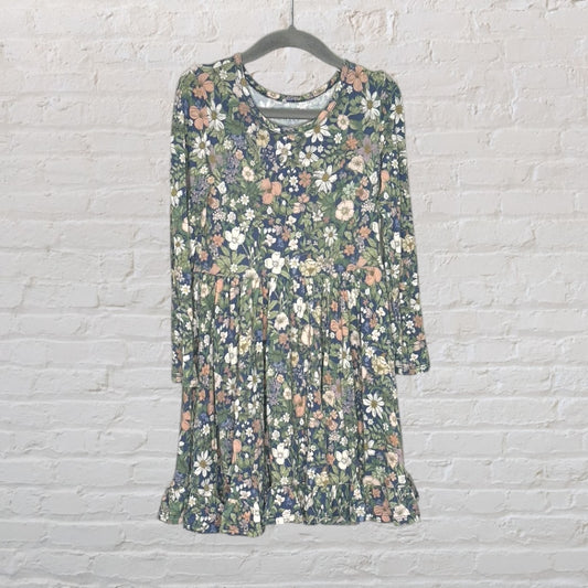 Women's long sleeve dress with a multicolored floral pattern on a green background, hanging against a white brick wall.