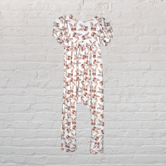 White long romper with brown bunny print and ruffled sleeves, displayed against a brick wall.