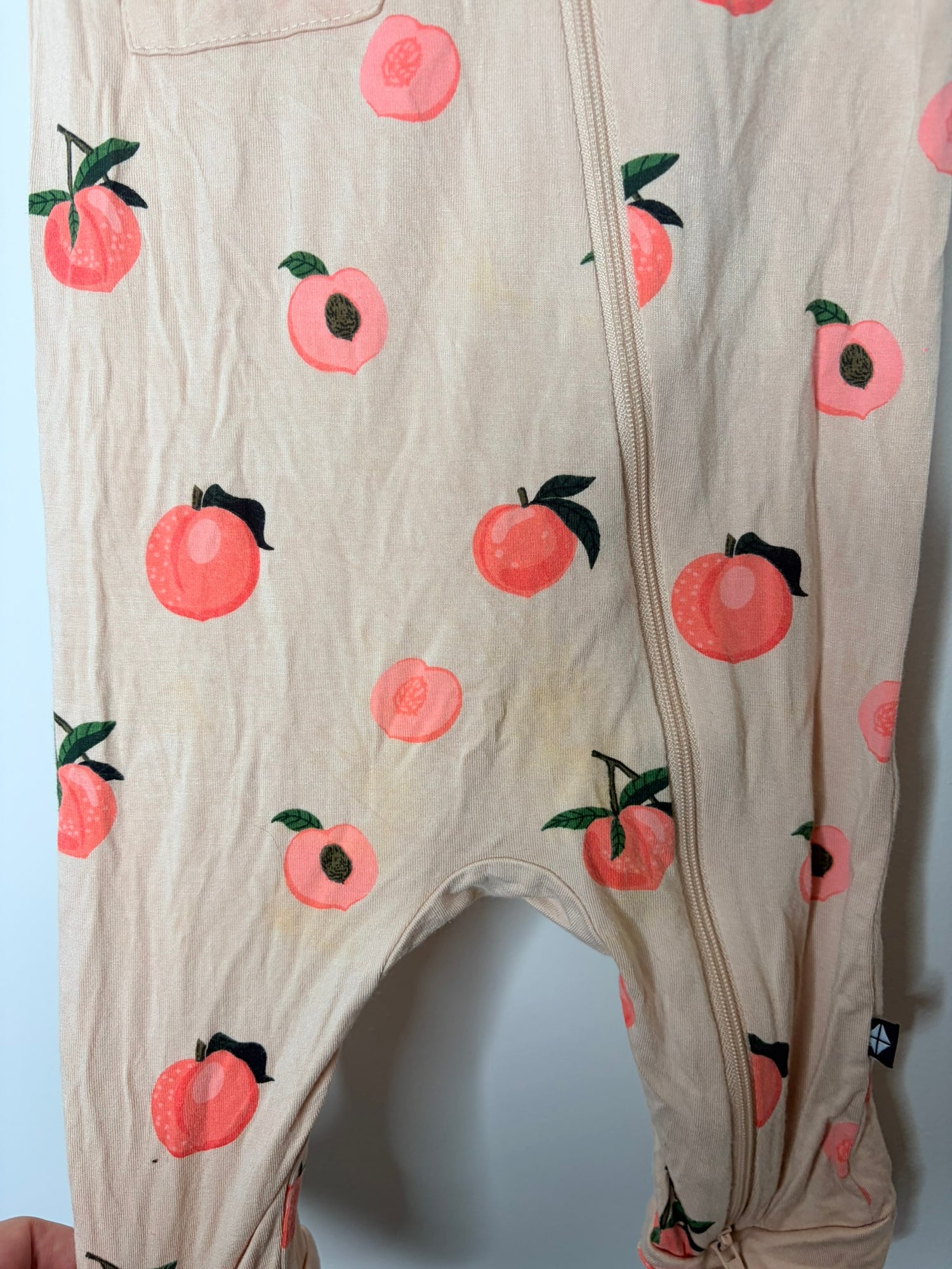 Beige sleeveless romper with peach print and front pocket, hanging on a gray hanger.