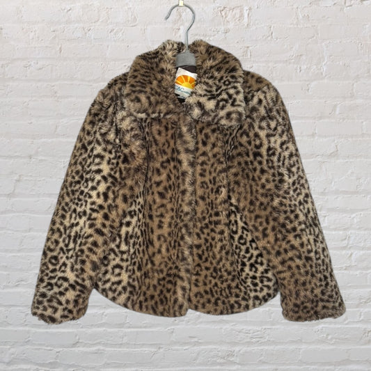Leopard print faux fur coat with a classic collar hanging on a hanger against a white brick wall.