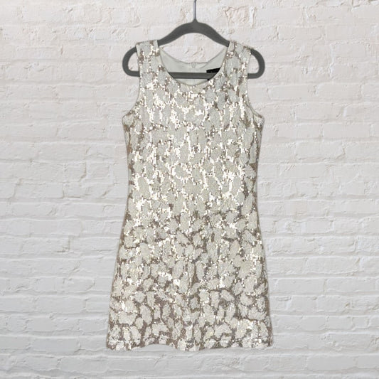 Silver sequin sleeveless mini dress hanging on a black hanger against a white brick wall.