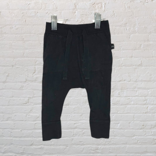 Children's black jogger pants with drawstring waist displayed on a hanger against a white brick background.