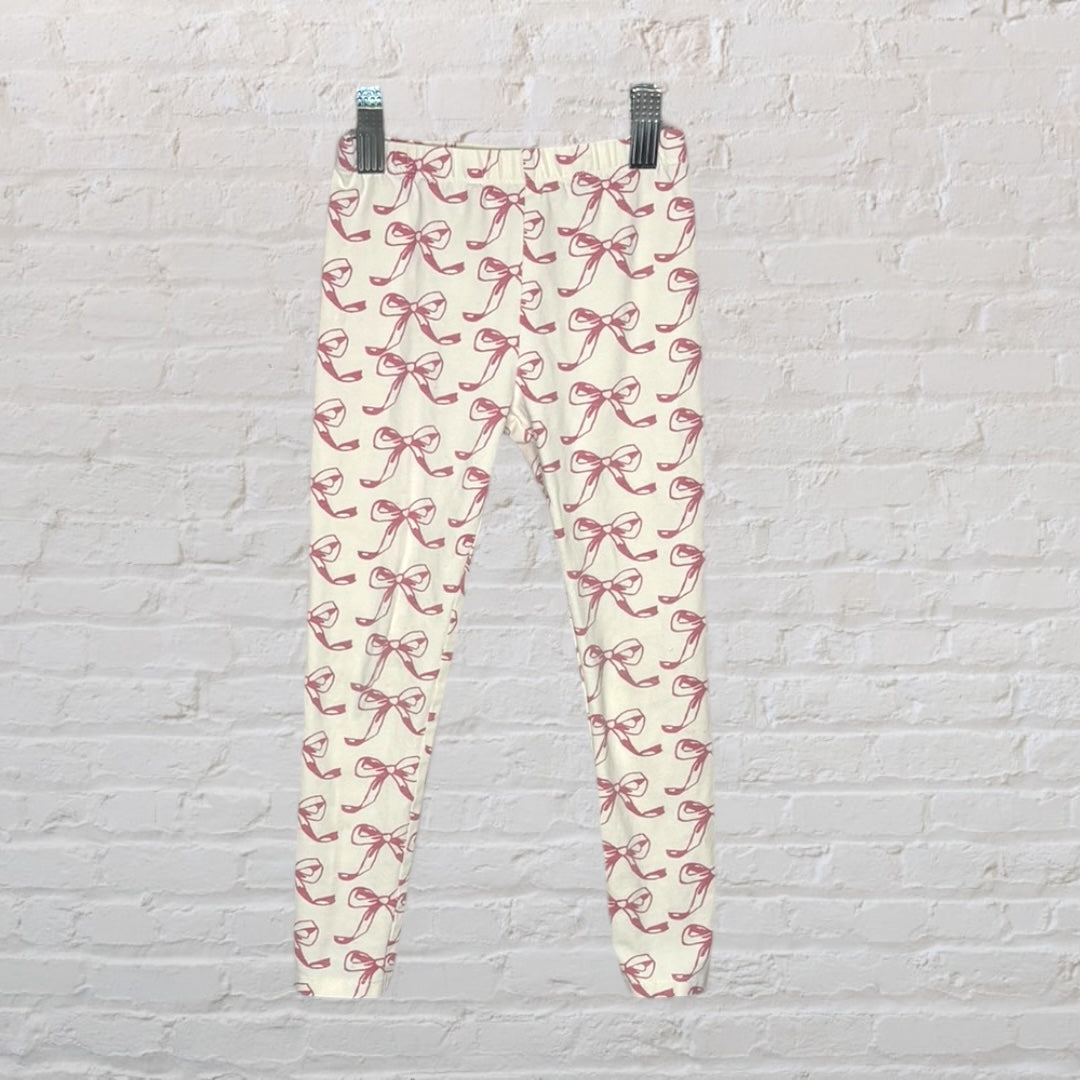 Cream leggings with pink bow print pattern hanging against a white brick wall.
