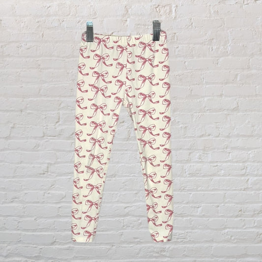 Cream leggings with pink bow print pattern hanging against a white brick wall.