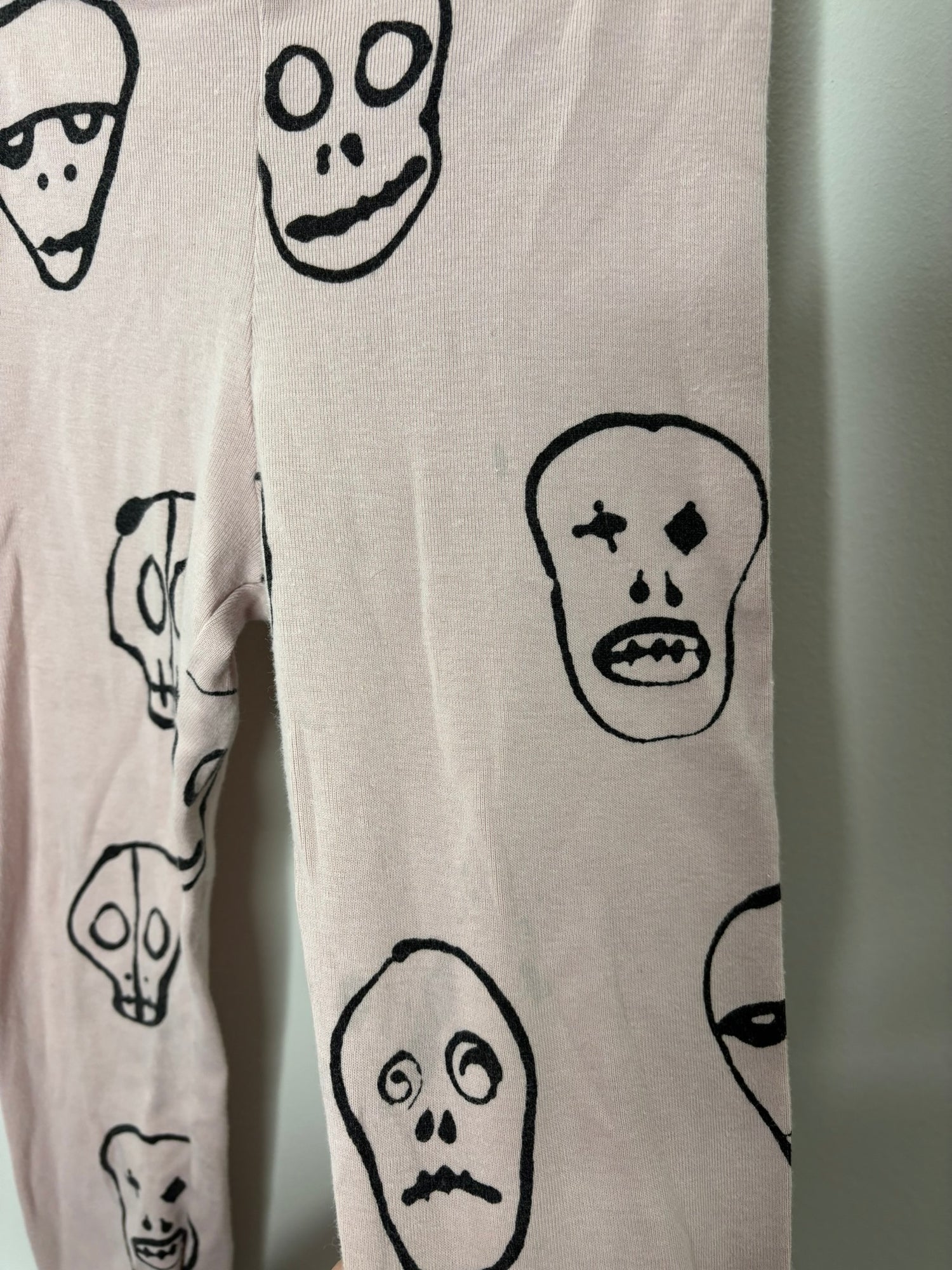 Pink leggings with black skull print design on a white brick wall background.
