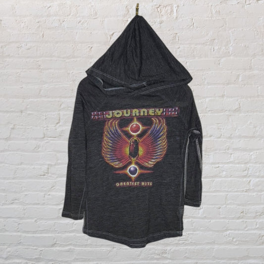 Dark grey hoodie featuring a colorful Journey Greatest Hits graphic, hanging against a white brick wall.