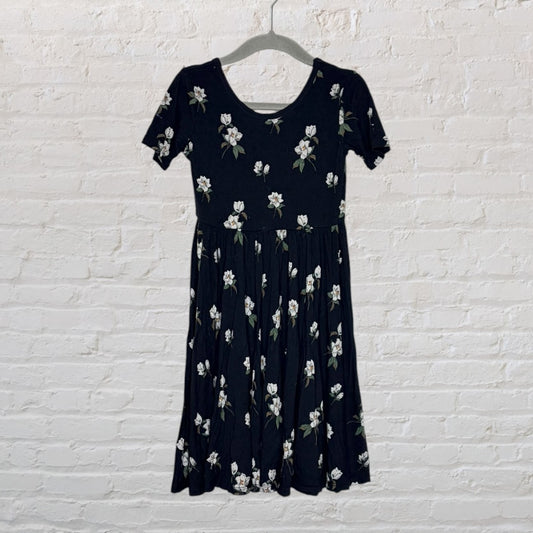 Black dress with white floral print and short sleeves, hanging against a white brick wall.