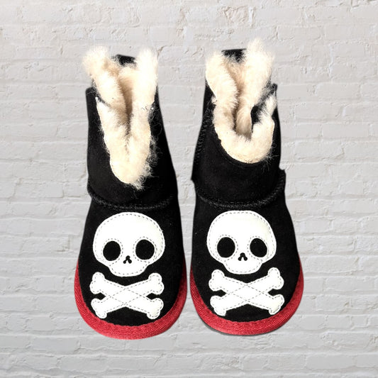 Pair of black shearling boots with white skull and crossbones design and red soles.