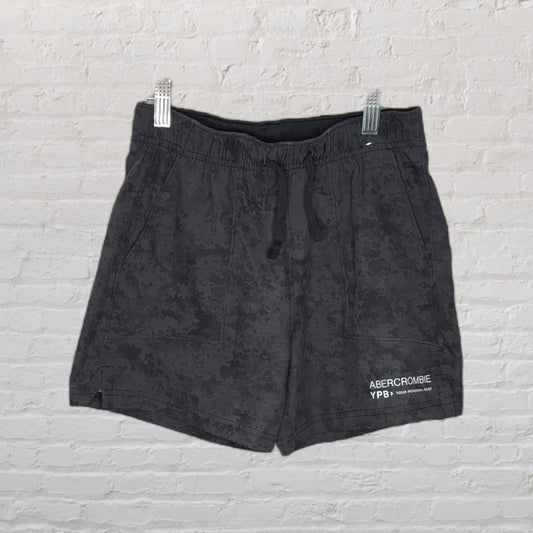 Dark grey Abercrombie athletic shorts with drawstring waist, featuring subtle text print, hanging against a brick wall.