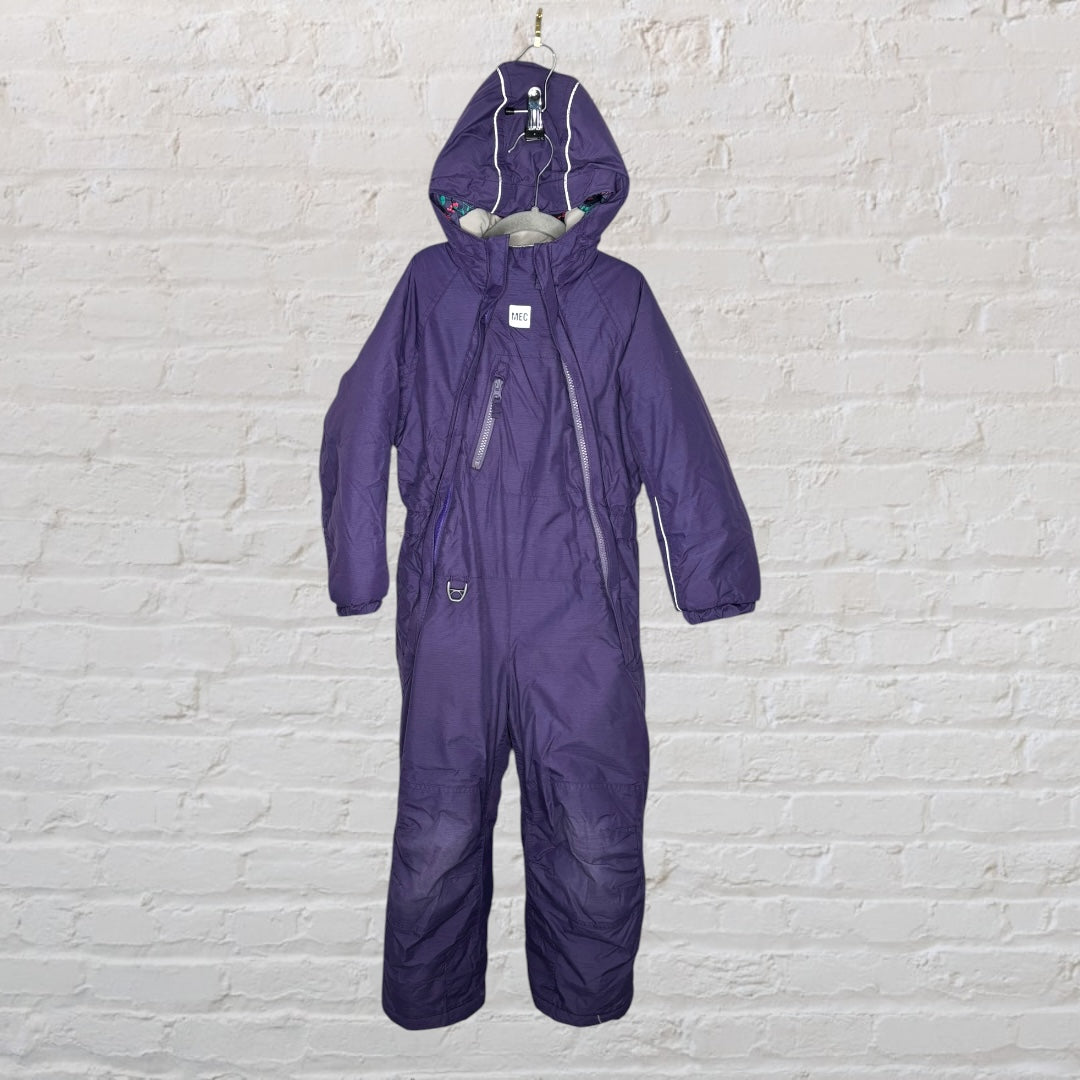 Purple insulated kids' snowsuit with hood and zip closure, hanging against a white brick wall.