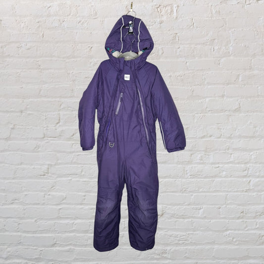 Purple insulated kids' snowsuit with hood and zip closure, hanging against a white brick wall.