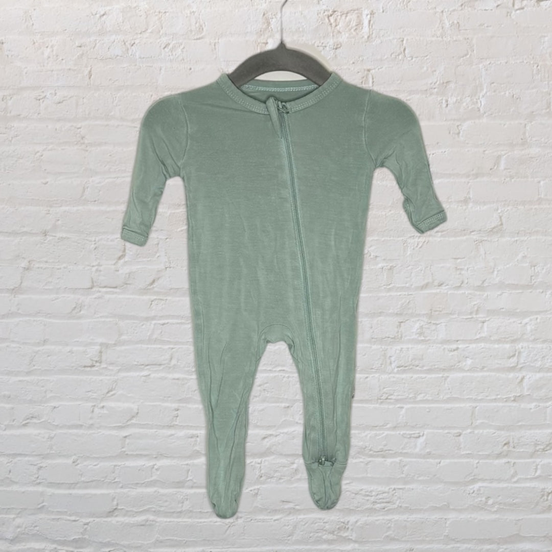 Sage green infant footed pajamas with a zip-up design, hanging on a hanger against a white brick wall.