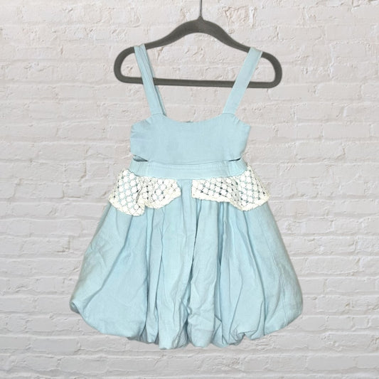 Light blue sundress with spaghetti straps and lace detail, displayed on a dark hanger against a white brick wall.