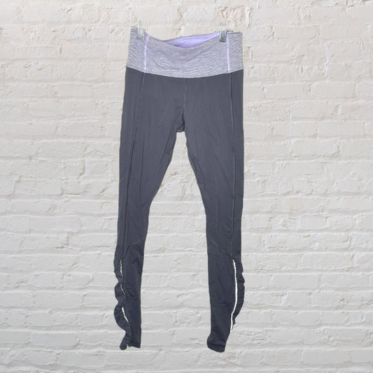 Dark grey high-waisted yoga leggings with light grey waistband, displayed against a white brick wall.
