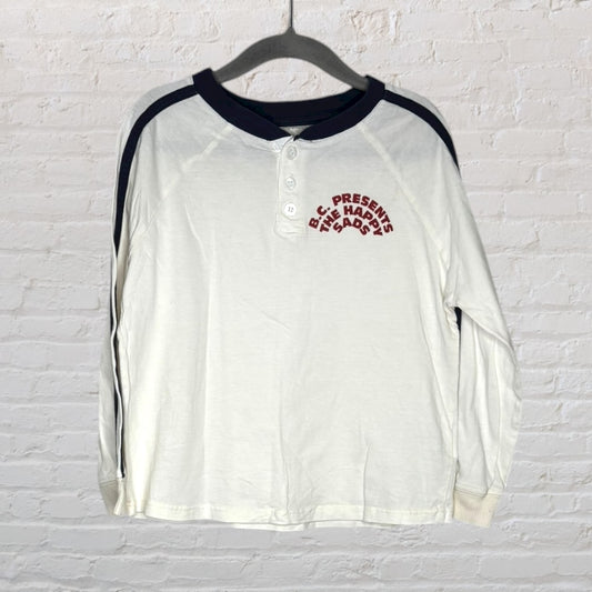 White and black raglan sleeve shirt with 'B.C. Presents The Happy Sad' text on the chest, hanging on a dark hanger.