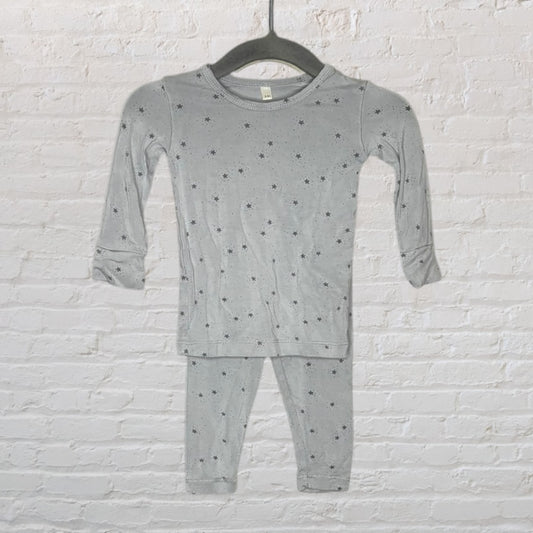 Grey pajama set with star pattern featuring long sleeves and pants, hanging on a black hanger against a white brick wall.