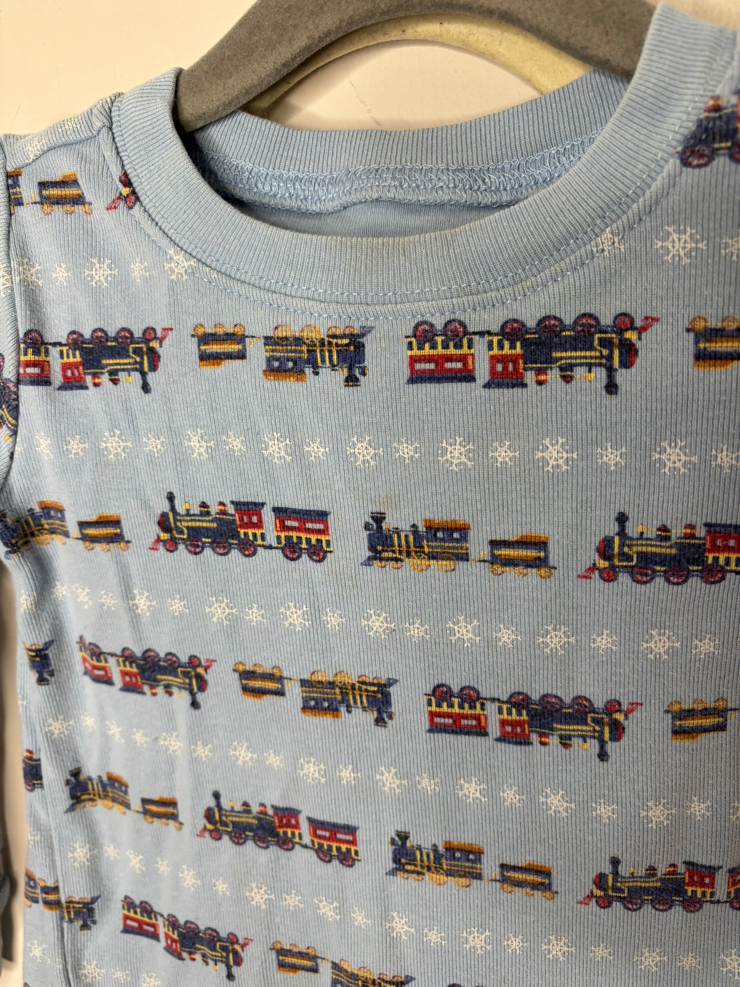 Light blue long-sleeve pajama set with colorful train patterns and snowflakes, hanging on a hanger.