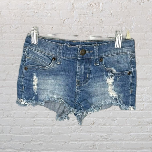 Blue distressed denim shorts with frayed hems and ripped details, hanging on a clip hanger.