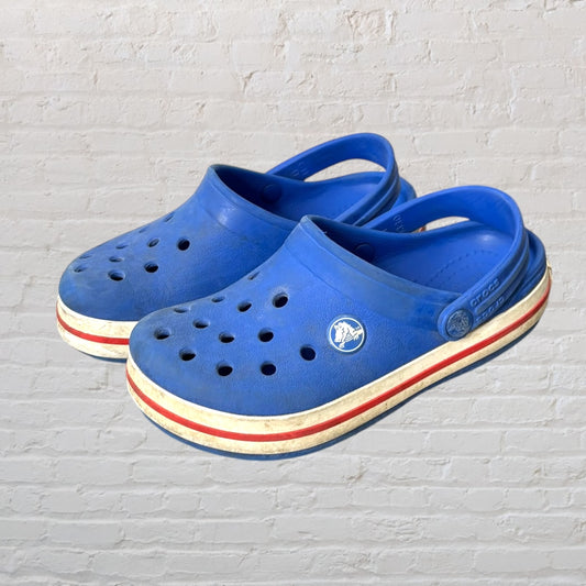 Pair of classic blue Crocs clogs with white and red striped soles.