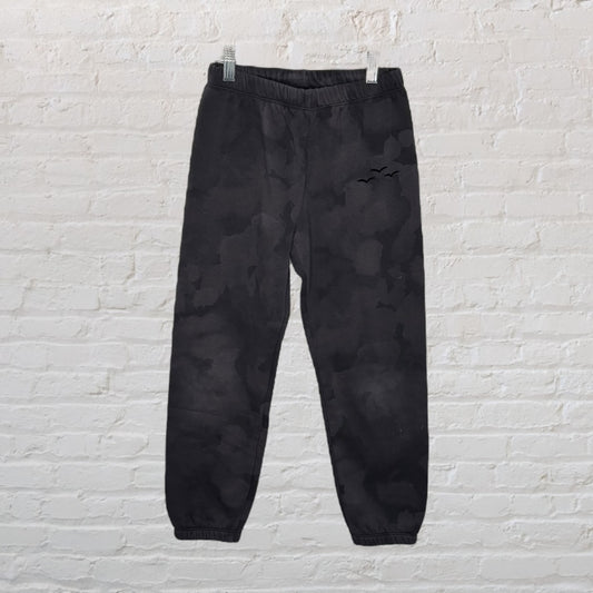 Dark camo jogger pants with elastic waistband and cuffs hanging against a white brick wall.