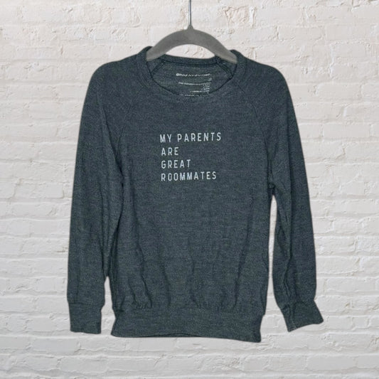 Dark grey sweatshirt with stylized text 'My Parents Are Great Roommates' hanging on a hanger against a brick wall.