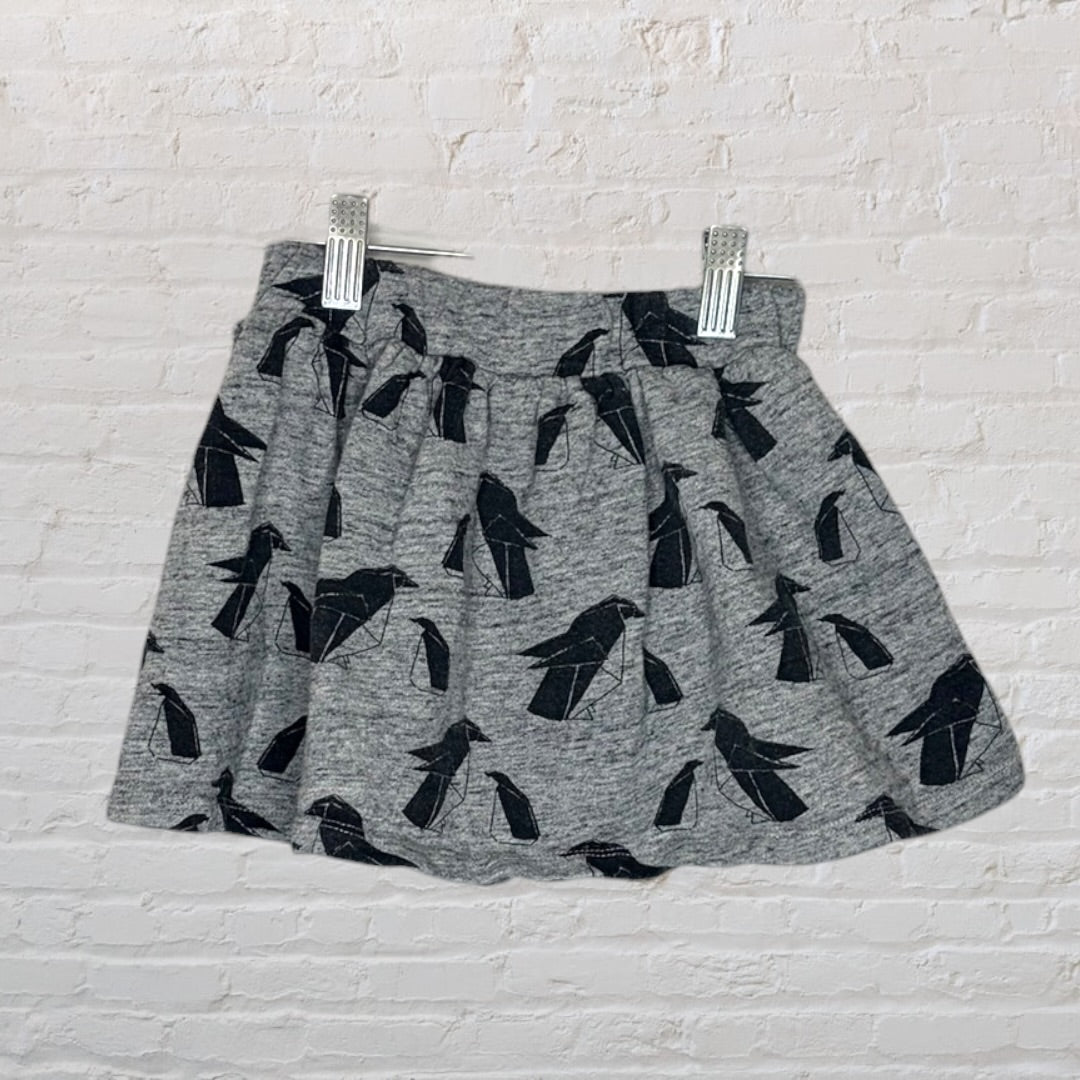 Grey skirt featuring a black bird print, displayed against a white brick wall, held by clips.