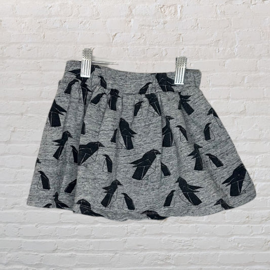 Grey skirt featuring a black bird print, displayed against a white brick wall, held by clips.
