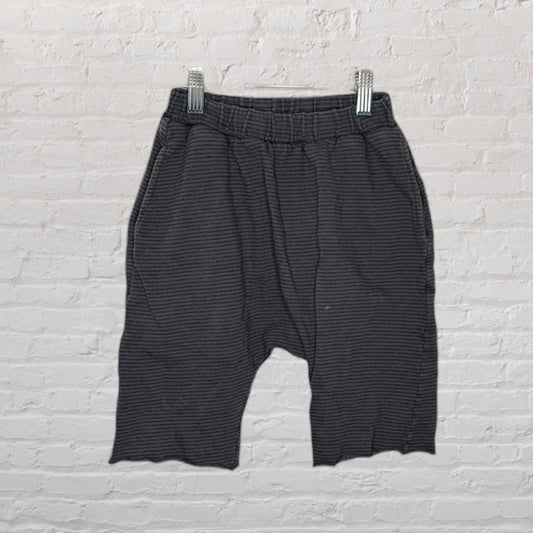 Dark grey casual striped drop-crotch shorts with an elastic waistband, hanging on a white brick wall.