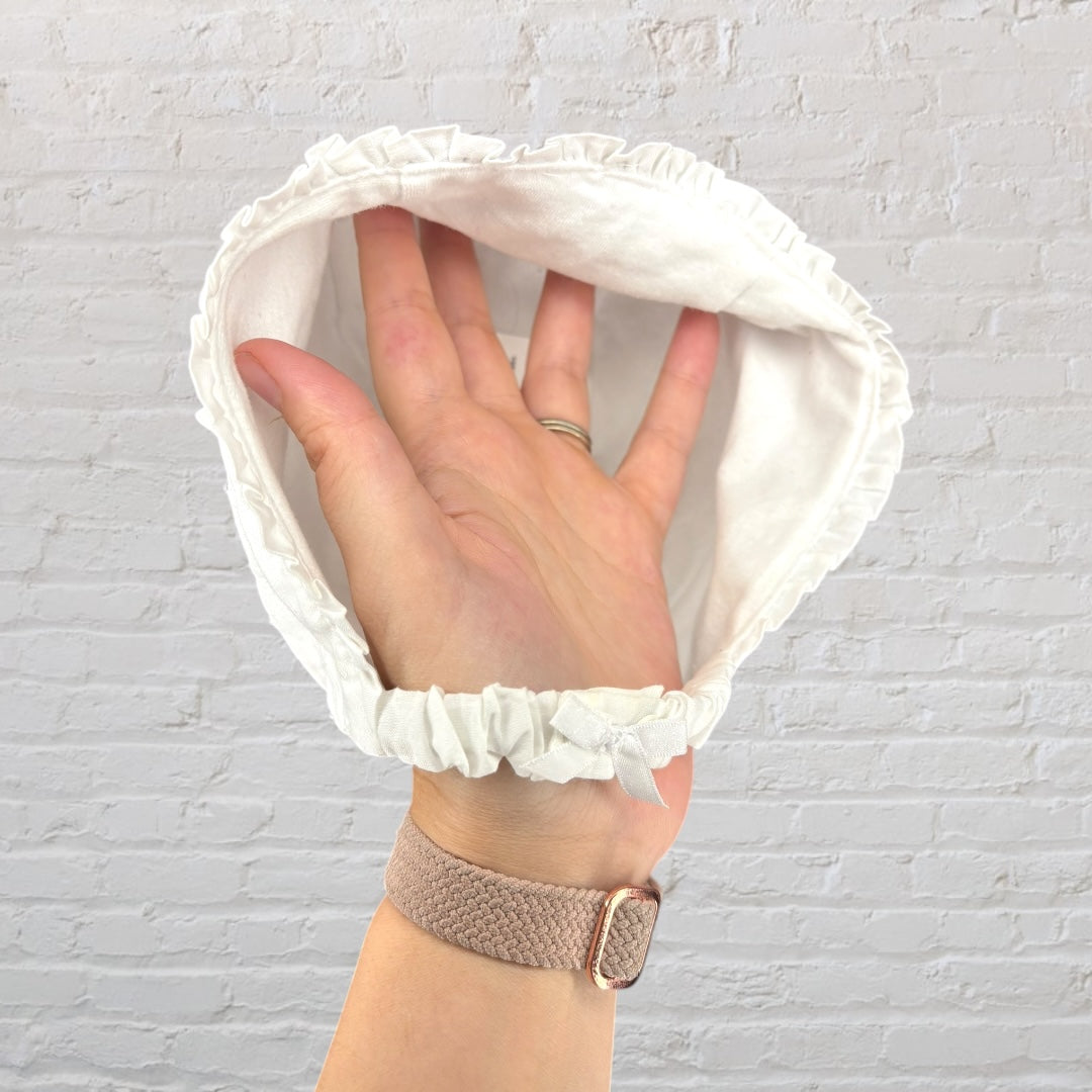 White vintage-style baby bonnet with delicate embroidery, held in front of a brick wall background.