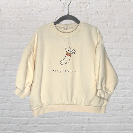 Cream sweatshirt with a cute bear in a stocking and 'Merry Christmas!' text, hanging on a hanger.