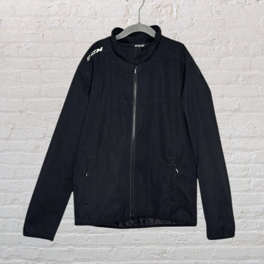 Black CCM full zip jacket with two zippered pockets and logo on the shoulder, displayed on a hanger.