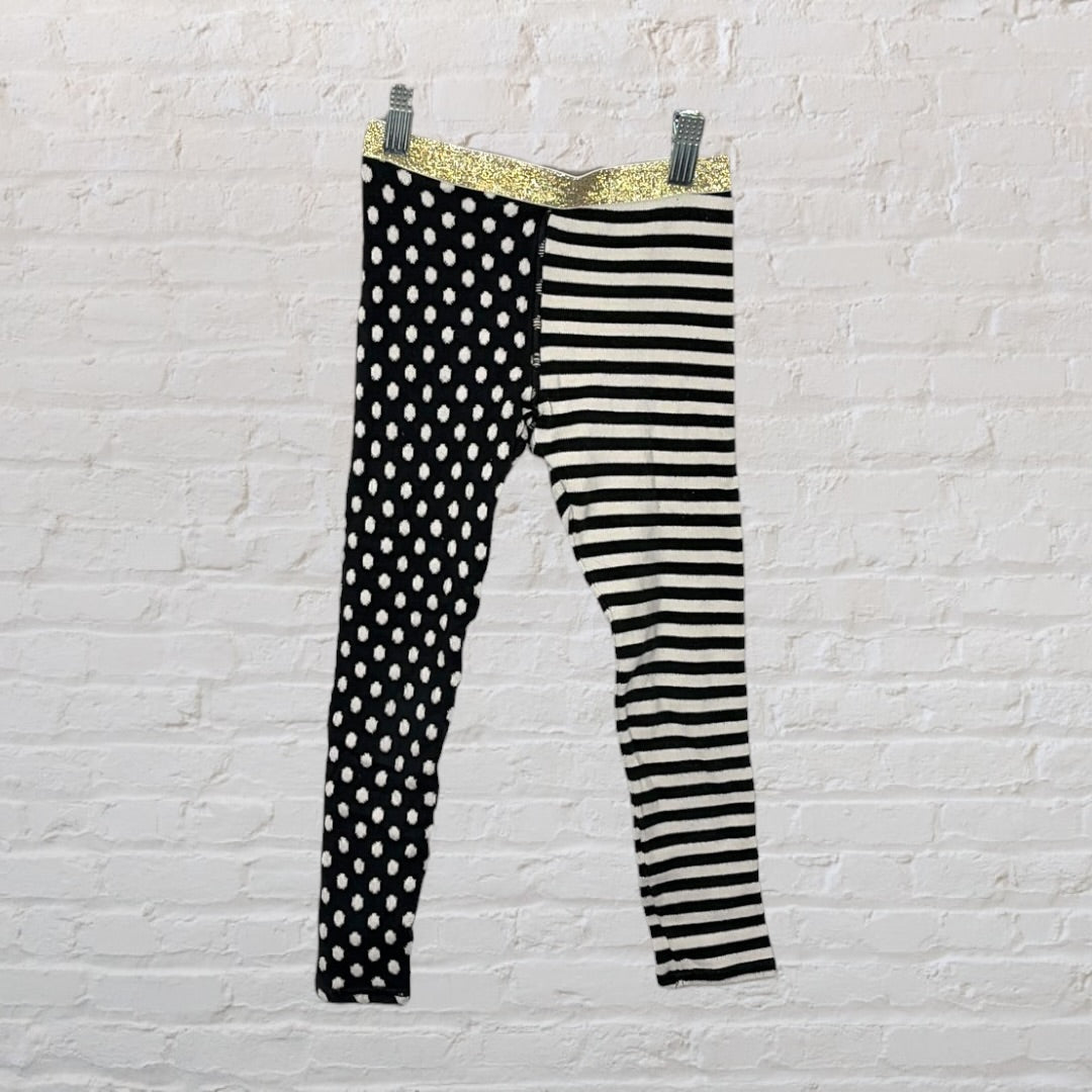 Black and white leggings with one leg in polka dots and the other in stripes, featuring a gold waistband.