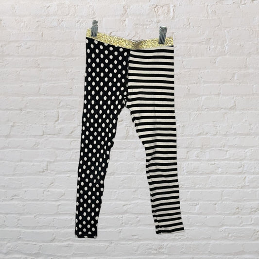Black and white leggings with one leg in polka dots and the other in stripes, featuring a gold waistband.