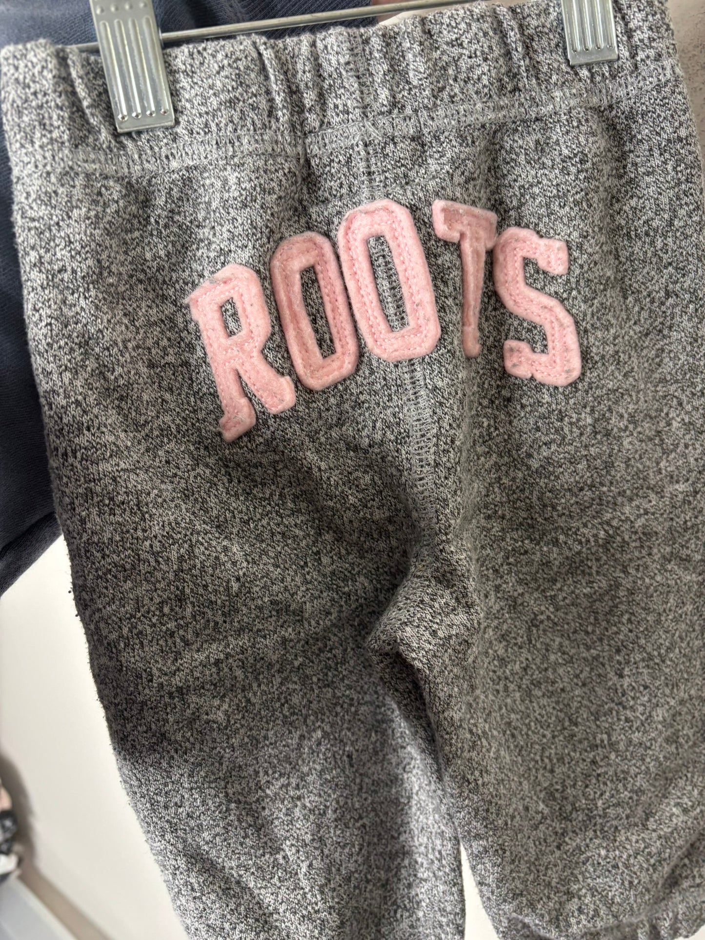 Heather grey Roots hoodie and pants set for kids with logo on the chest, displayed against a brick wall.