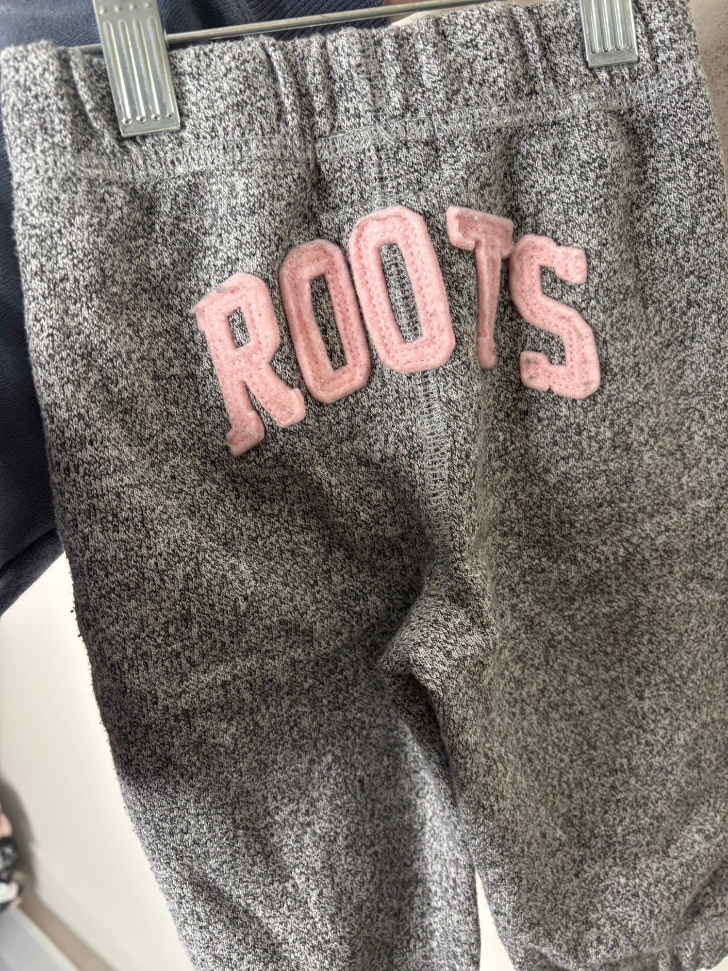 Heather grey Roots hoodie and pants set for kids with logo on the chest, displayed against a brick wall.