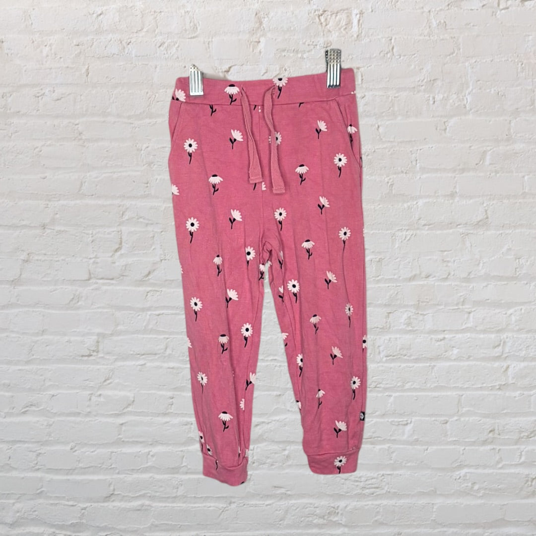 Pink pajama set with white floral design on a hanger against a white brick wall.