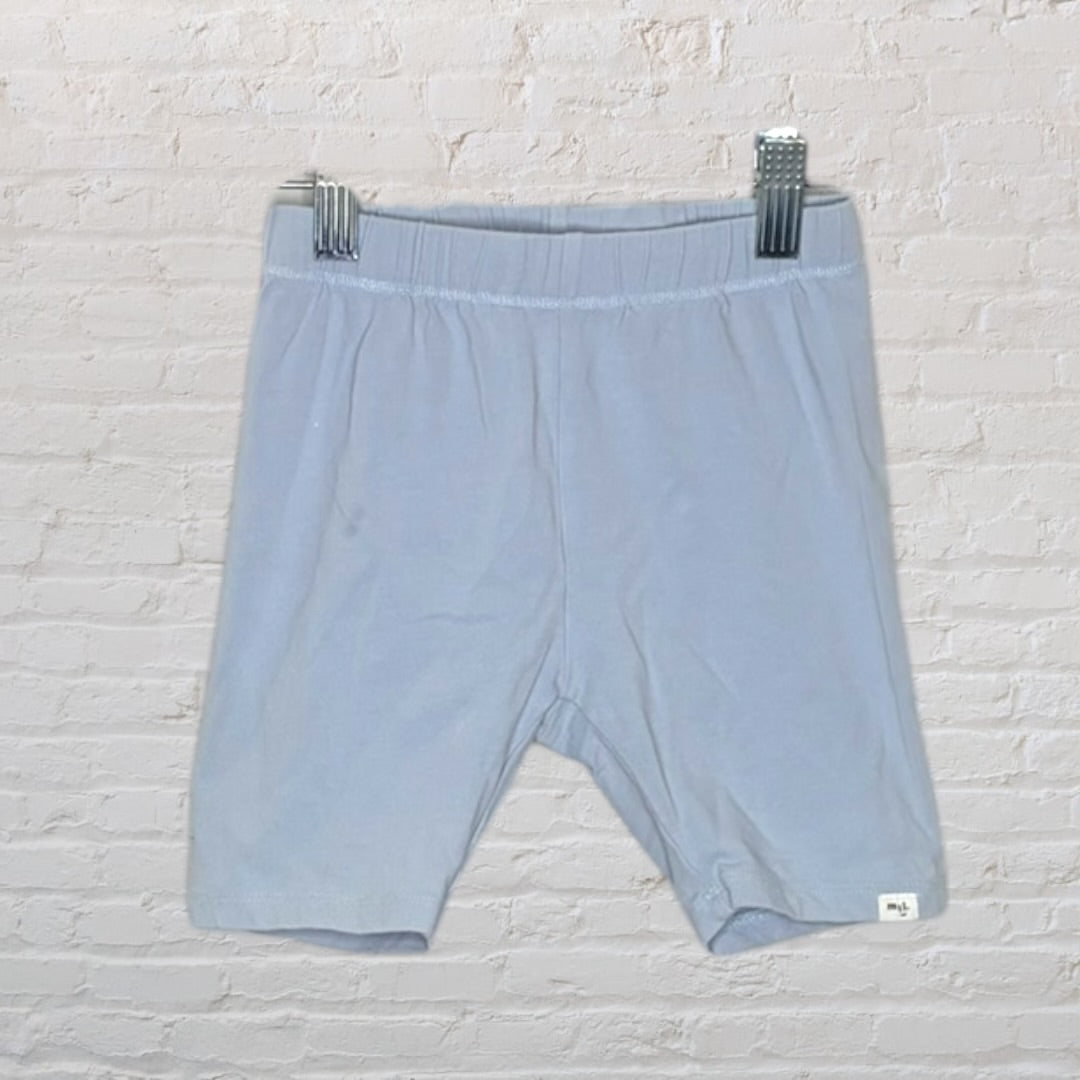 Light blue unisex shorts on hangers against a brick wall background.