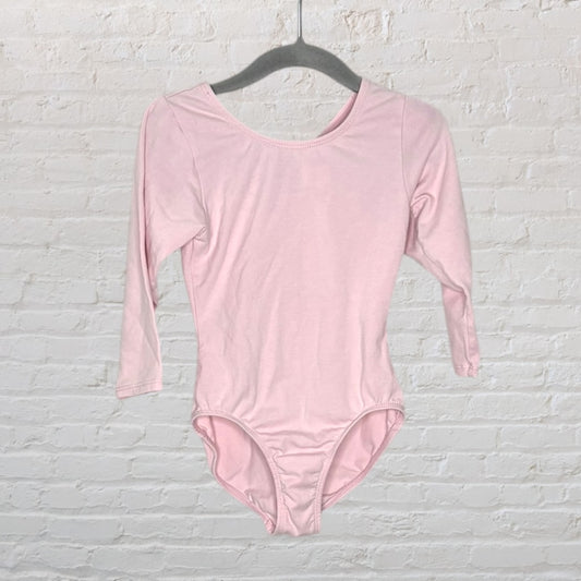 Light pink long sleeve leotard on a hanger against a white brick wall background.