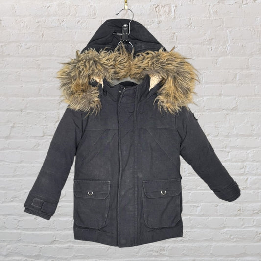 Black long parka with faux fur hood hanging against a brick wall.