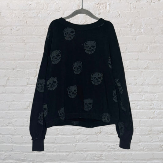 Black sweater with grey skull print pattern hanging on a hanger against a white brick wall.