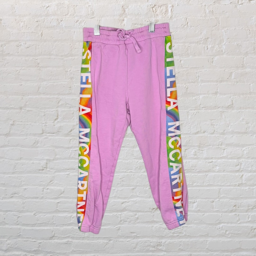 Pink tracksuit set with a hoodie and pants featuring rainbow Stella McCartney logos along the sleeves and legs.