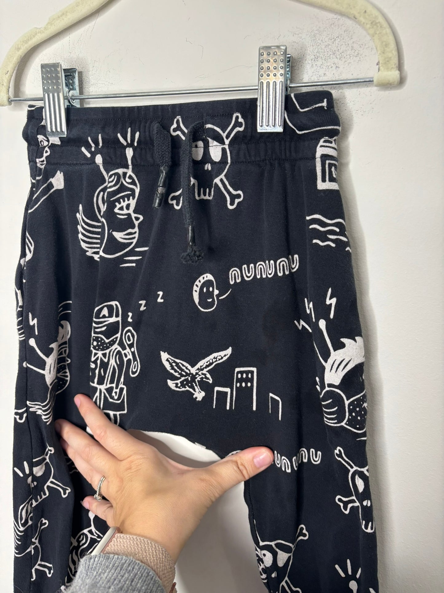 Black harem pants with white doodle print design, displayed against a brick wall.