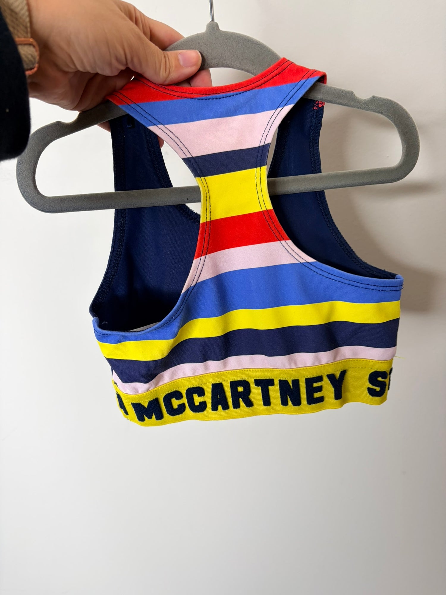 Navy blue sports bra for kids with red shoulder accents and yellow logo band by Stella McCartney Kids.