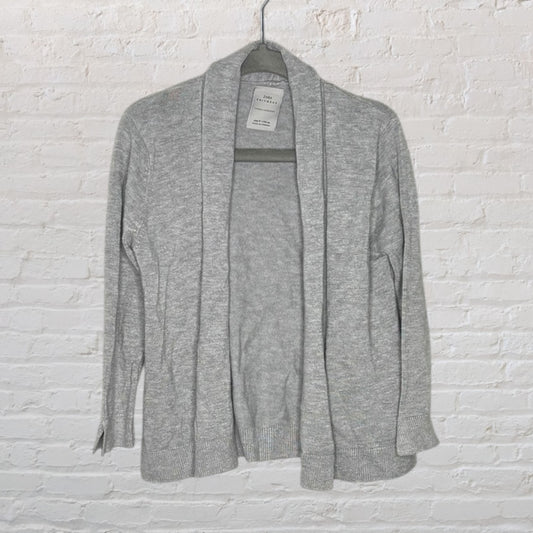 A gray open-front cardigan from ZARA Knitwear hanging against a white brick wall.