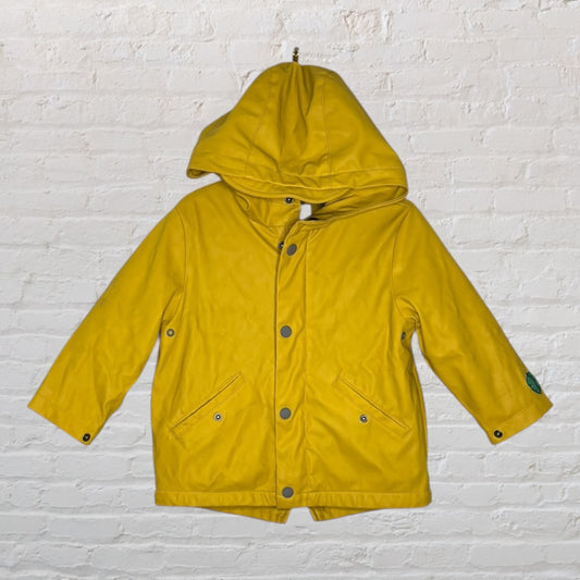 Bright yellow children's rain jacket with hood and front pockets, against a white brick wall.