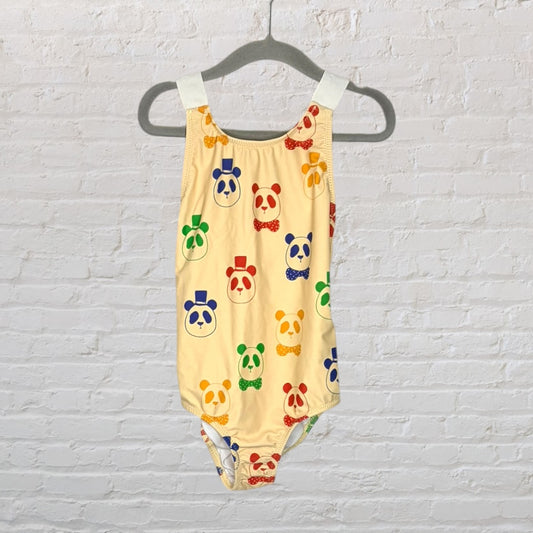 Yellow one-piece swimsuit with colorful panda faces wearing hats and bow ties, hanging on a hanger.