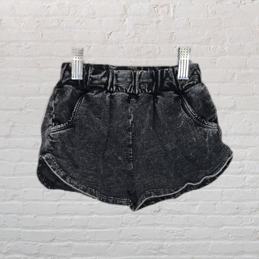 Washed black high-waisted denim shorts with elastic waistband, displayed against a brick background.