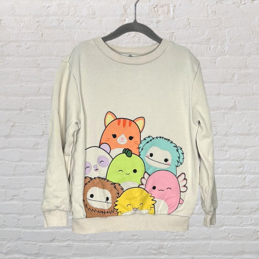 Off-white sweatshirt with a graphic of colorful cartoon animal characters on a hanger against a white brick wall.